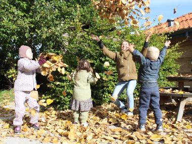 Børn og voksne har gang i en dejlig efterårsleg med blade på legepladsen